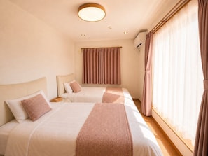 A hotel room with two beds, a window with sheer curtains, and a ceiling light.