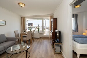 Ein Hotelzimmer mit Sofa, Esstisch mit Stühlen, Fernseher und Bett, mit Blick auf die Stadt.