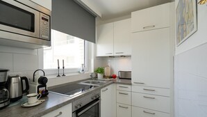 Moderni keittiö, jossa on sisäänrakennettu mikroaaltouuni, liesi ja uuni, ikkunasta avautuva kaunis näkymä ja valkoiset kaapit.