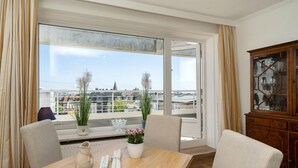 Hotellihuone, jossa on parveke, ruokapöytä tuoleineen, lasiovilla varustettu kaappi ja ruukkukasveja.