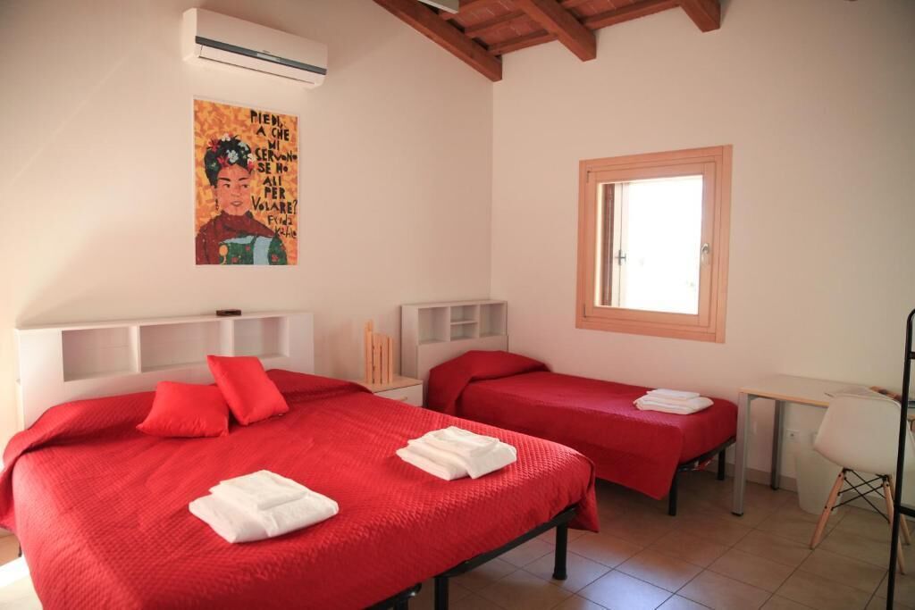 Quarto de hotel com duas camas, uma escrivaninha, uma cadeira, uma janela e um quadro na parede.