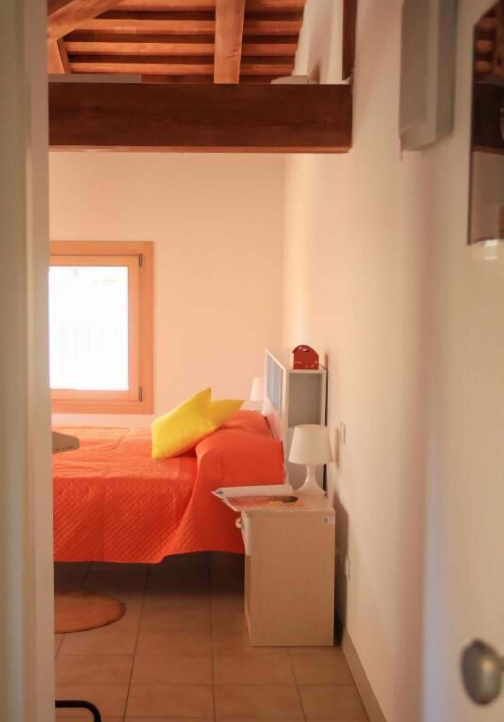 Un dormitorio con cama, mesita de noche, lámpara y ventana.