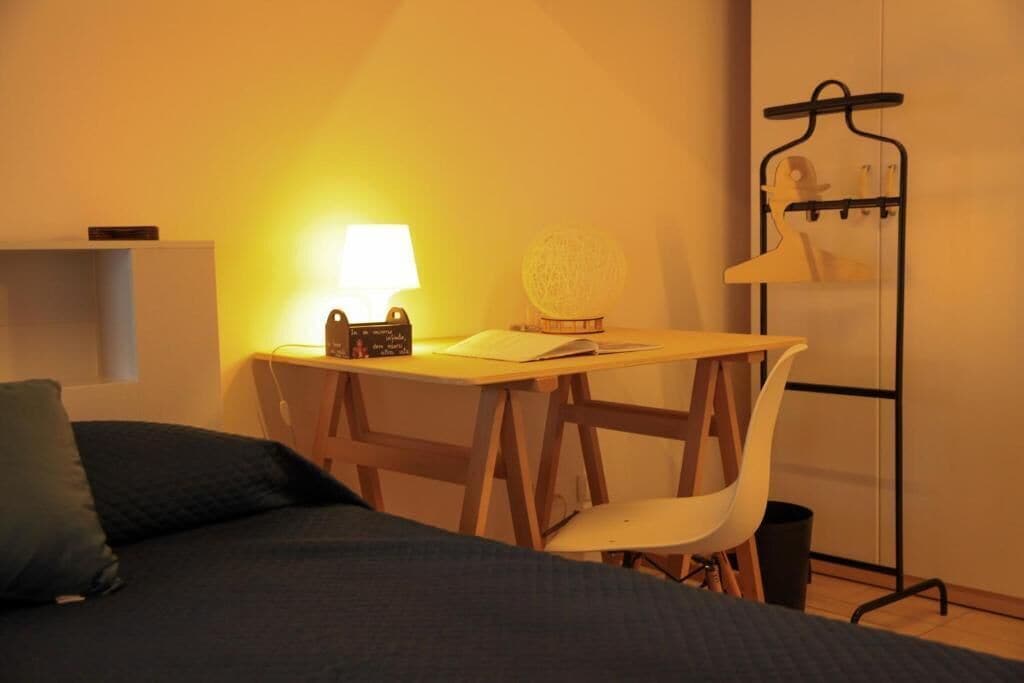 Une chambre à coucher avec un lit, un bureau avec une lampe, une chaise, une petite table avec un globe terrestre et un porte-manteau.