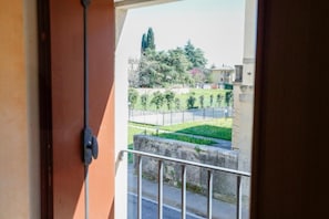 Un balcón con vistas a un parque verde, una valla y edificios al fondo.