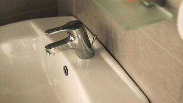 A bathroom sink with a mirror above it, a toilet paper roll on a shelf, and a soap dispenser.