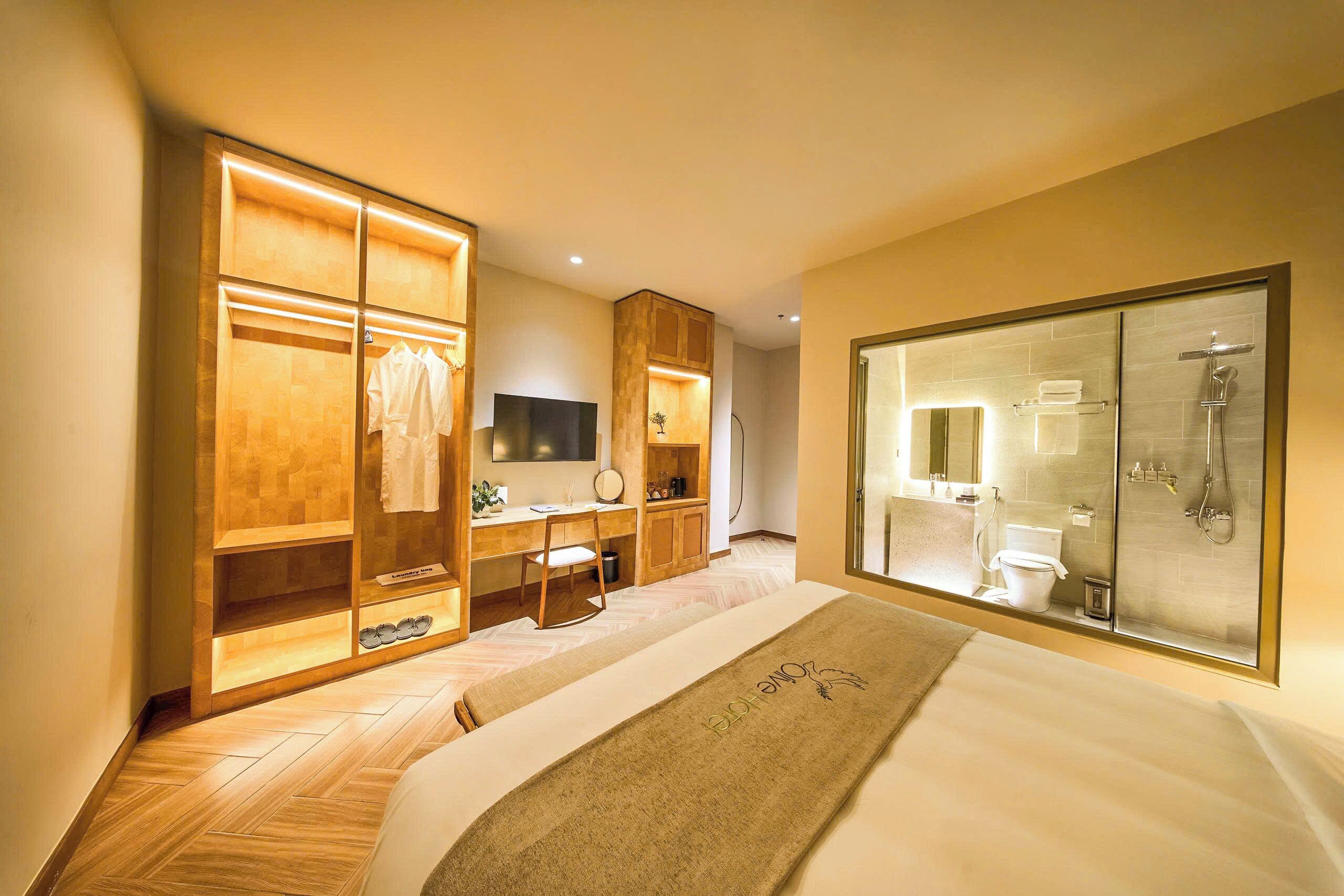 Une chambre d’hôtel comprenant un lit, une armoire, un bureau avec une chaise, une télévision et une salle de bain avec une douche en verre.