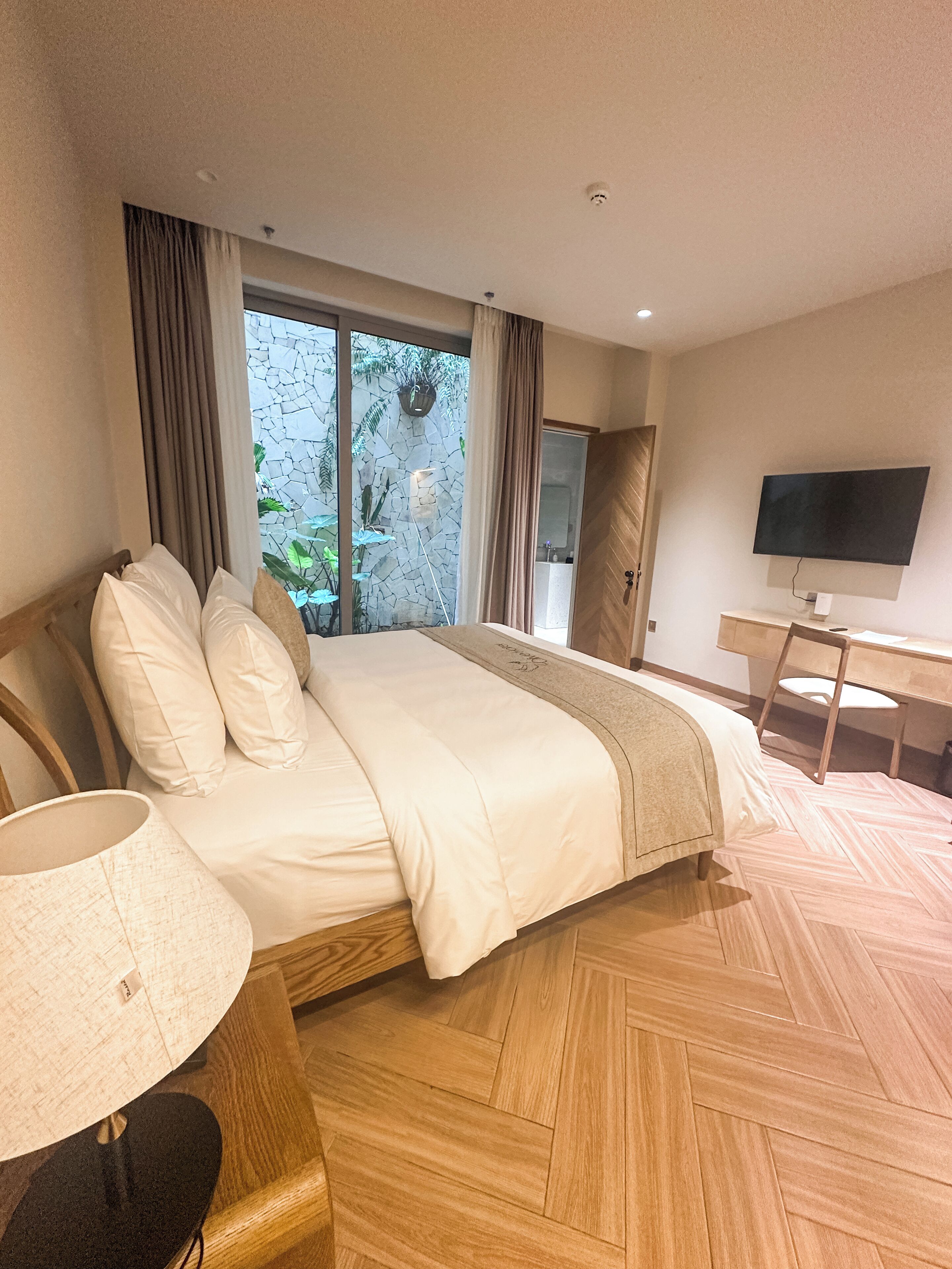Une chambre d’hôtel équipée d’un lit, d’une télévision, d’un bureau et offrant une vue sur la verdure par la fenêtre.