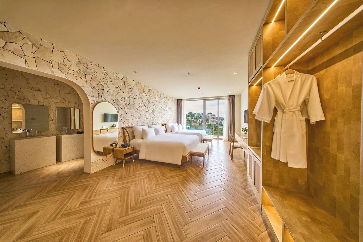 Habitación de hotel moderna con pared de piedra, una cama grande, tocador con espejo y una bata colgada en la pared.