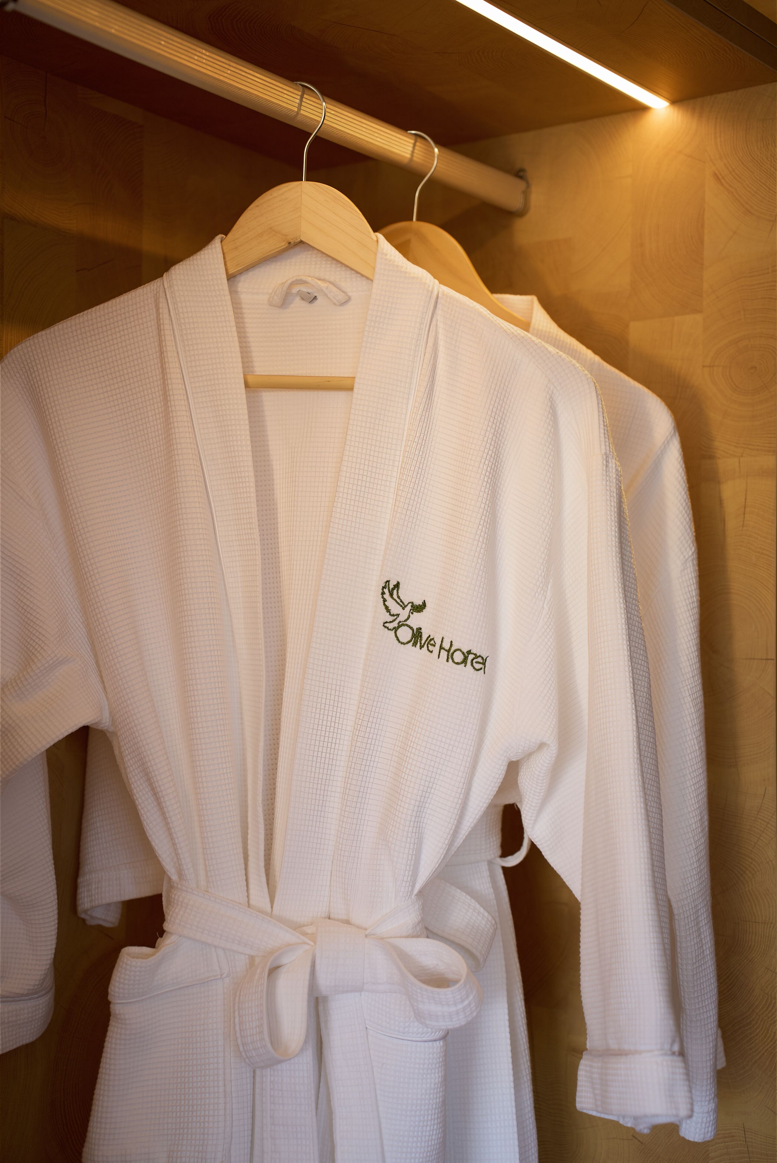 A white robe with a logo on the chest, hanging on a wooden hanger.