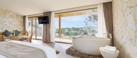 A modern bedroom with a large bed, a bathtub, and a view of the city.