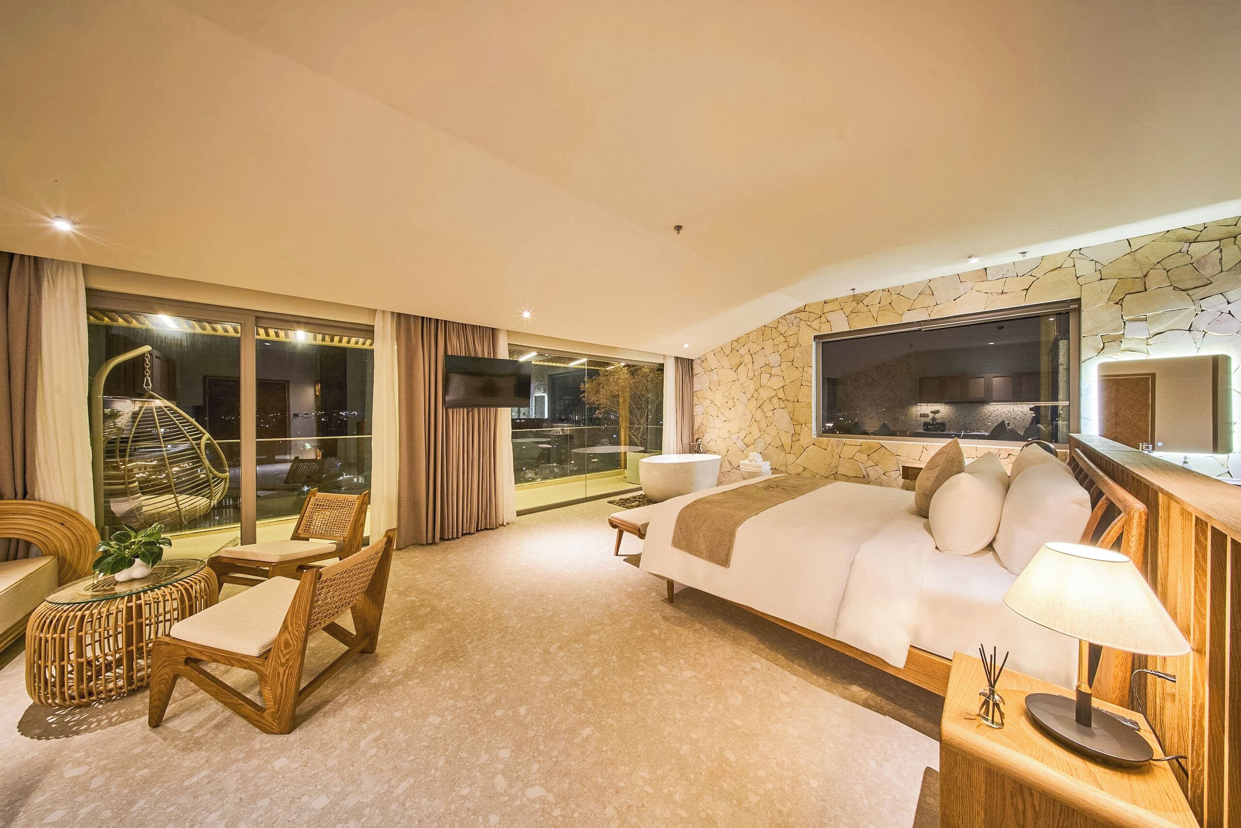 Une chambre d’hôtel moderne dotée d’un grand lit, d’une télévision, d’un balcon avec une porte vitrée et d’un mur en pierre.
