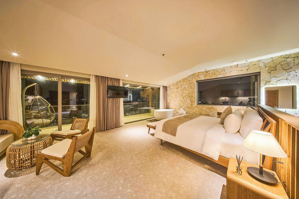 Une chambre d’hôtel moderne dotée d’un grand lit, d’une télévision, d’un balcon avec une porte vitrée et d’un mur en pierre.