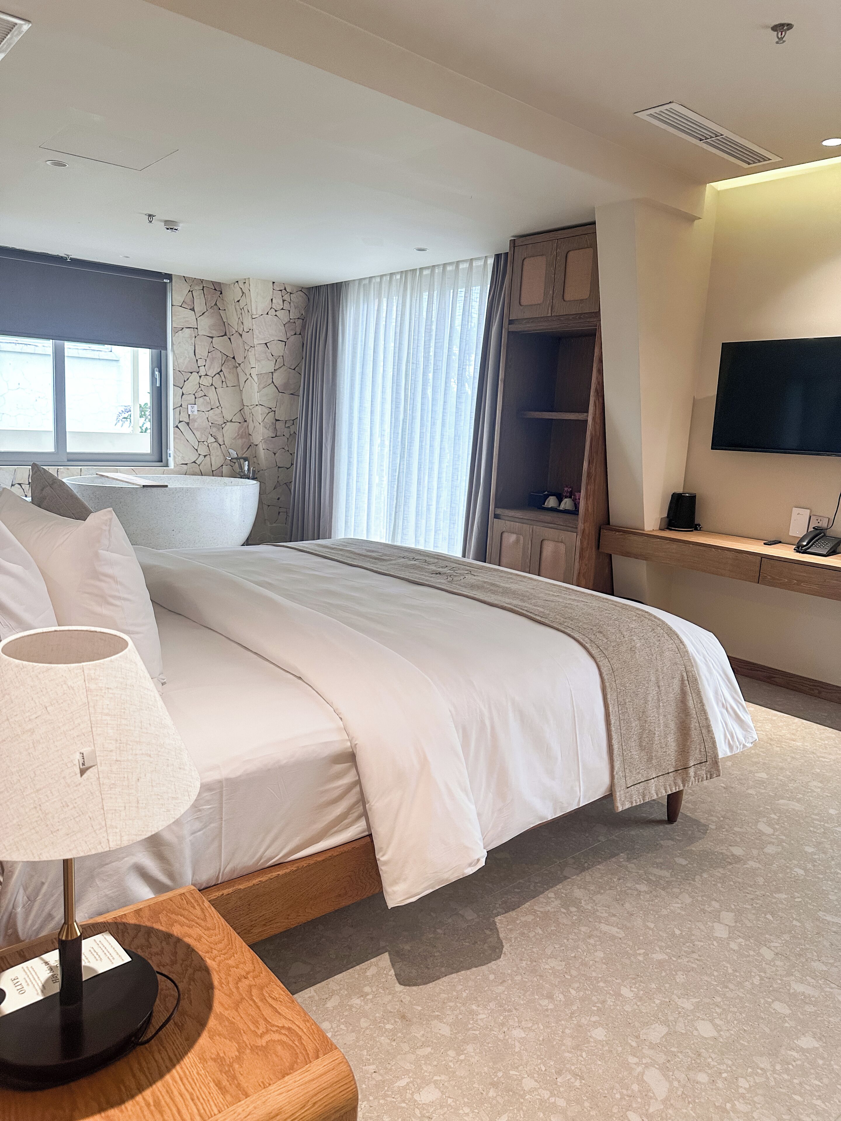 Une chambre d’hôtel moderne dotée d’un grand lit, d’une table de chevet avec une lampe, d’une télévision et d’une salle de bain avec baignoire.