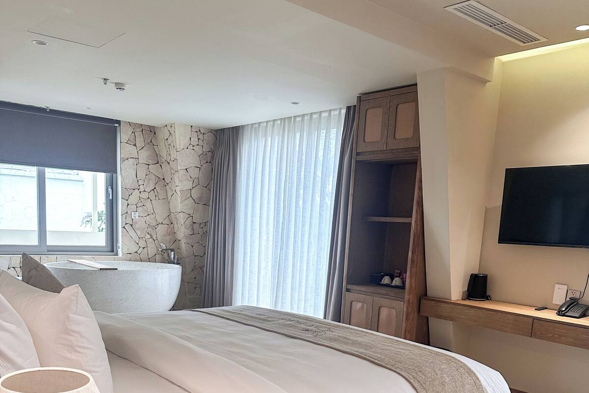 Une chambre d’hôtel moderne dotée d’un grand lit, d’une table de chevet avec une lampe, d’une télévision et d’une salle de bain avec baignoire.