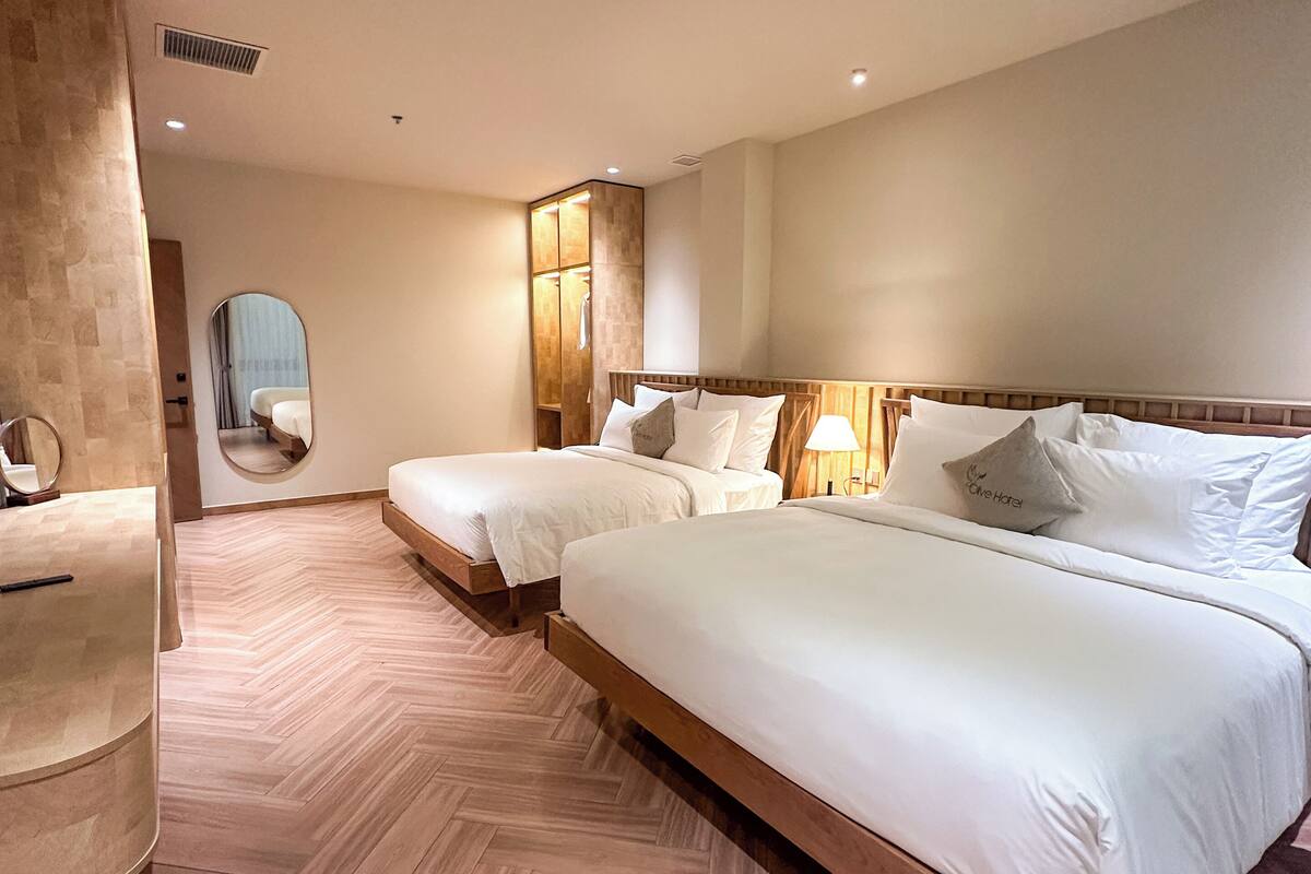 Une chambre d’hôtel avec deux lits, un miroir, une coiffeuse et un parquet à motifs en chevrons.