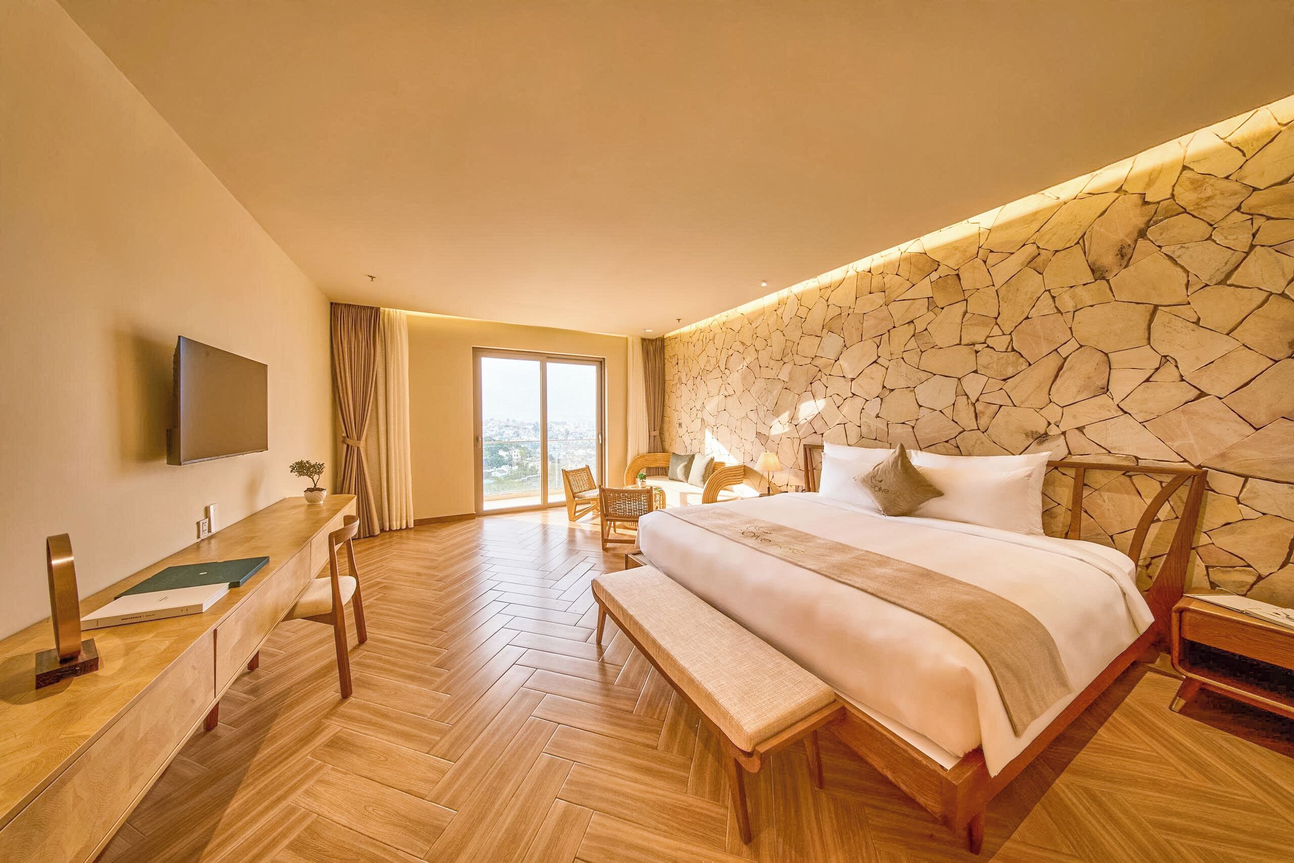Une chambre d’hôtel avec un grand lit, un bureau avec une chaise, une télévision et un mur en pierre.