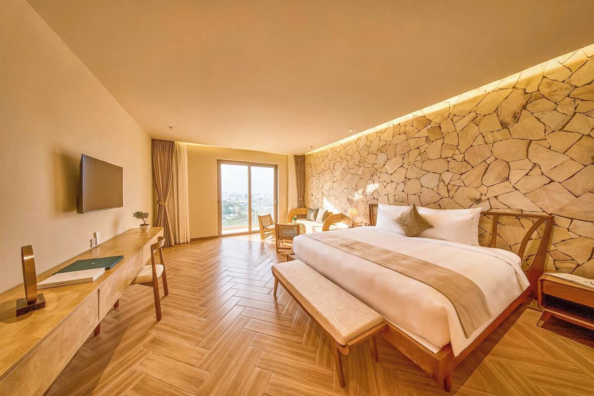 Habitación de hotel con una cama grande, un escritorio con silla, televisión y pared de piedra.