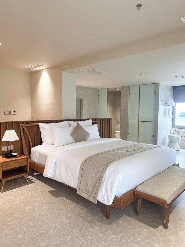Ett modernt hotellrum med en stor säng, sängbord, en bänk, en spegel och en duschhörna.
