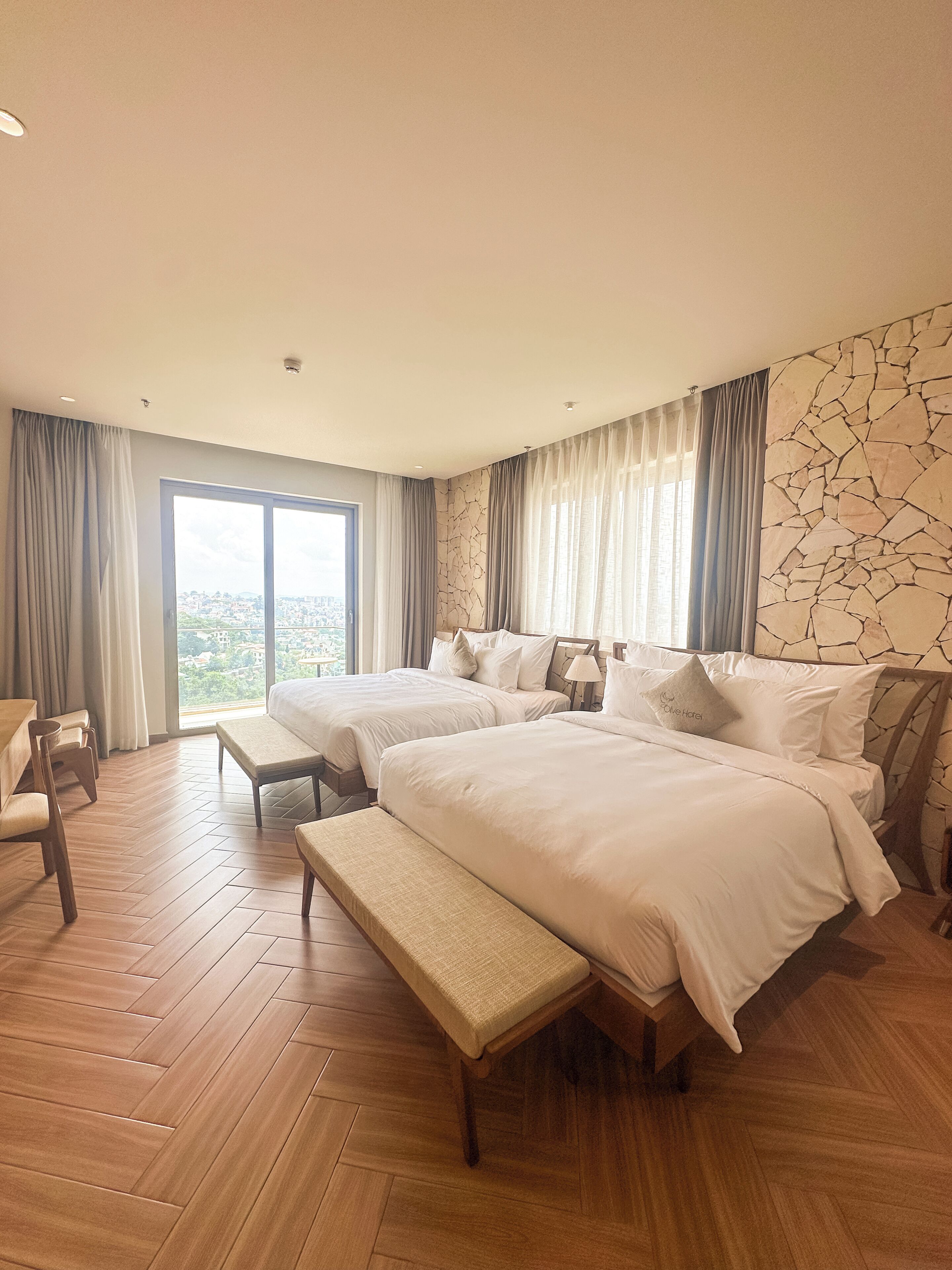 Une chambre d’hôtel avec deux lits, un banc, un bureau et une vue sur la ville.