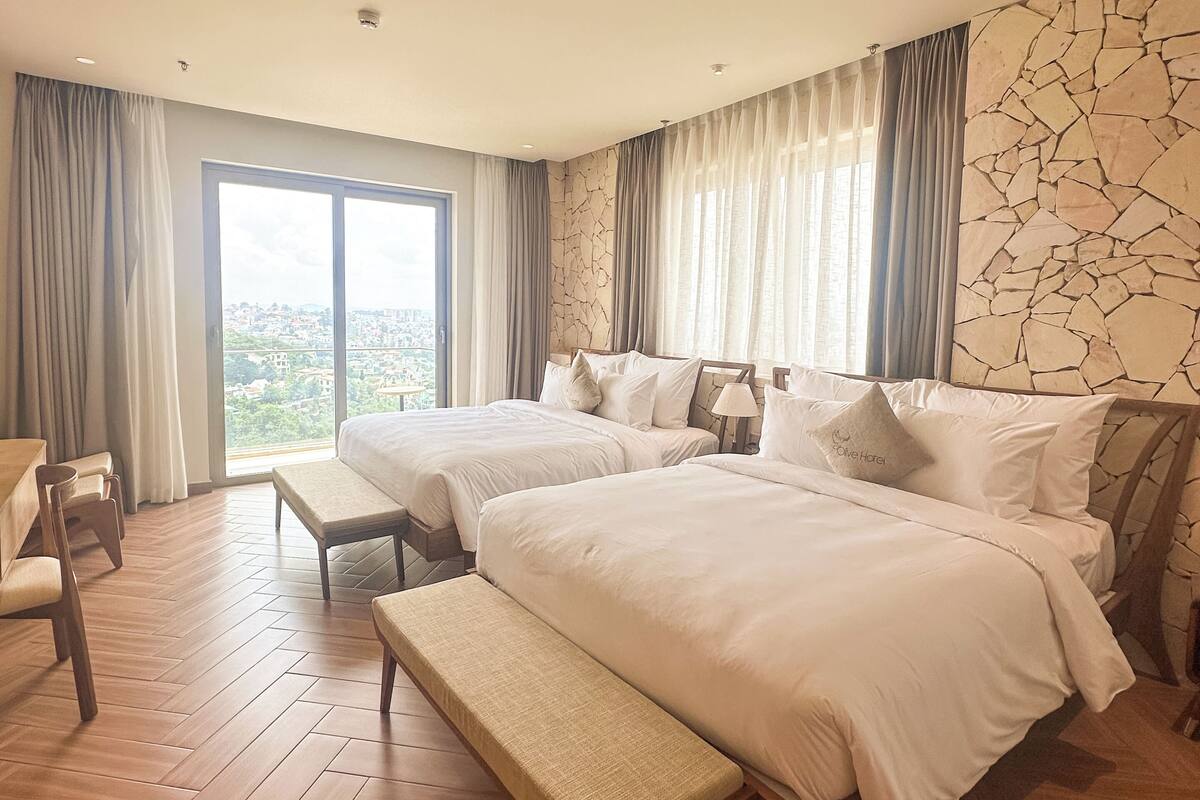 Une chambre d’hôtel avec deux lits, un banc, un bureau et une vue sur la ville.