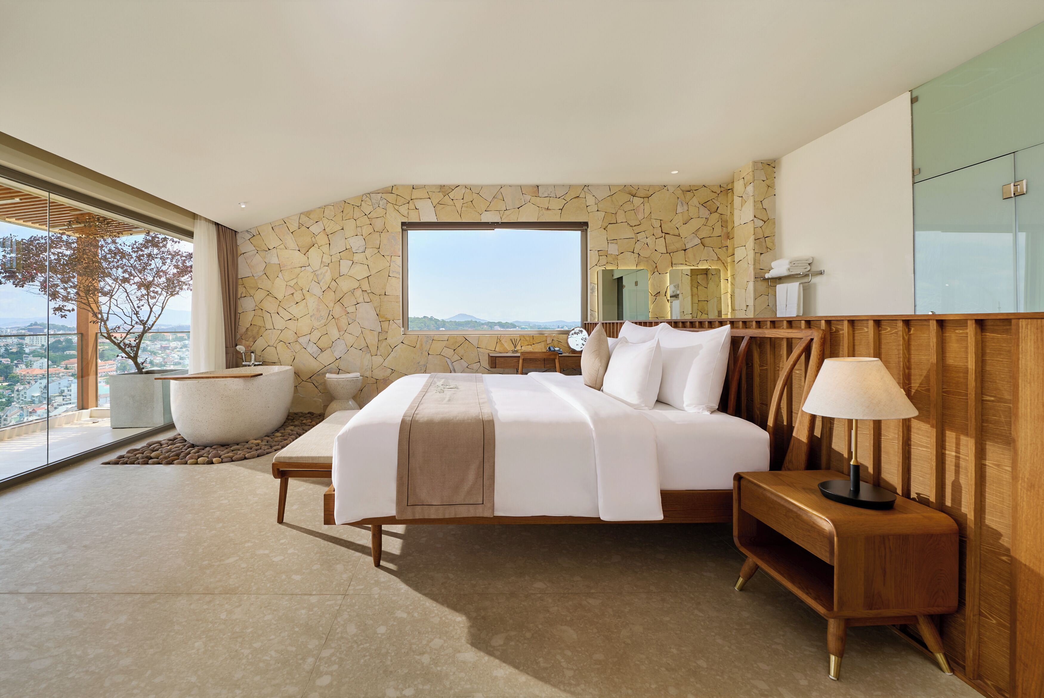 Quarto moderno com cama grande, mesa de cabeceira, janela e vista para a cidade.