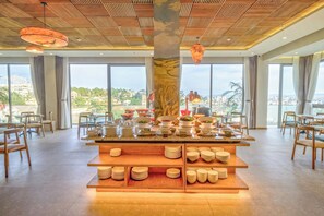 Un espace de restauration moderne doté d’un îlot central, de plusieurs configurations de sièges et de grandes fenêtres offrant une vue sur la ville.