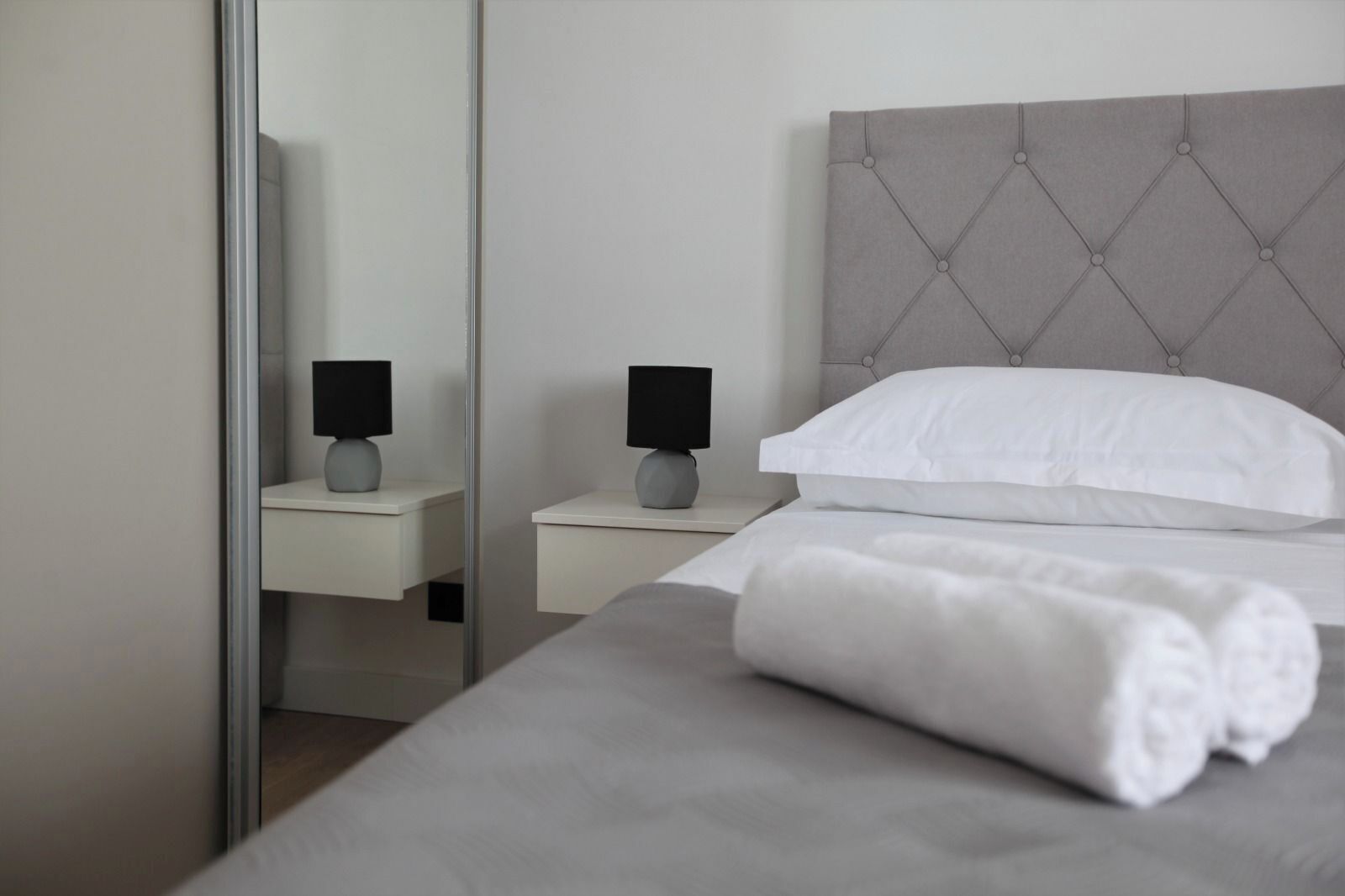A modern hotel room with a large bed, two bedside tables, and a mirror.