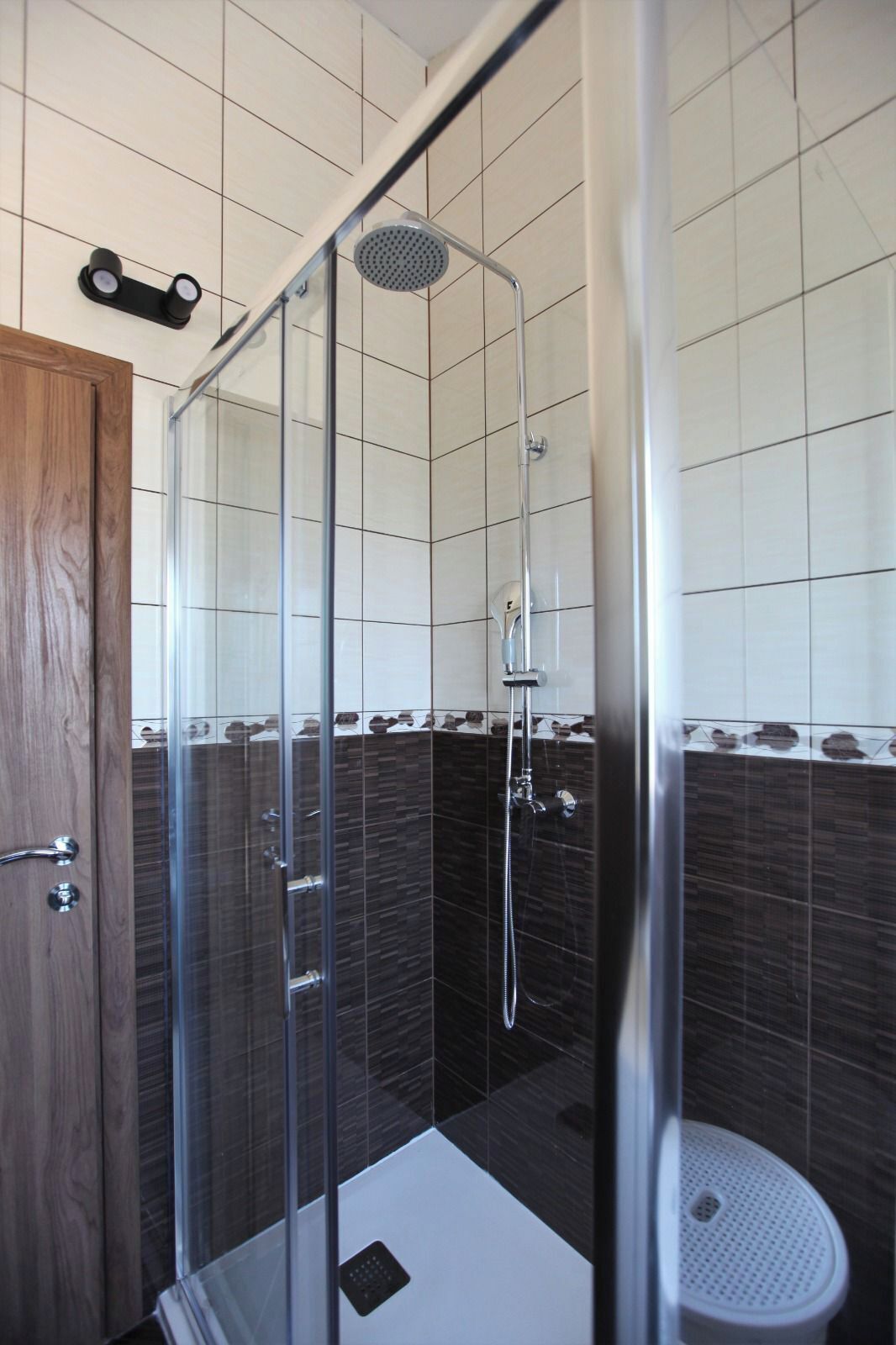 Een douchecabine met glazen wanden, een handdouche, een glazen deur en een witte betegelde muur.