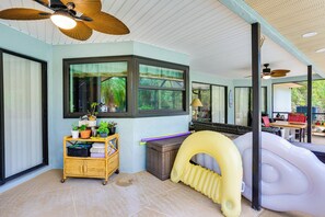 A room with a large window, ceiling fans, a wicker cart with plants, and an inflatable slide. - Heated Pool & Resort-Style Perks! Punta Gorda Home (Punta Gorda)