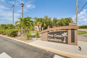 A sign for 'Deep Creek Gardens' with a palm tree symbol, surrounded by greenery and a clear sky. - Heated Pool & Resort-Style Perks! Punta Gorda Home (Punta Gorda)