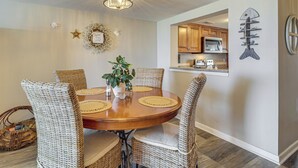 Een eetgedeelte met een ronde tafel, rieten stoelen, een kroonluchter en een keuken op de achtergrond.