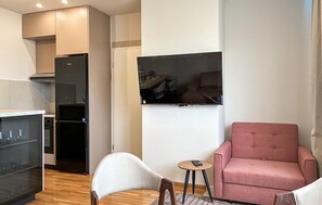 A modern living room with a flat-screen TV, a pink armchair, a small round table, and a kitchen area with a refrigerator and cabinets. - Nice apartment in Krvavac II with WiFi (Krvavac II)