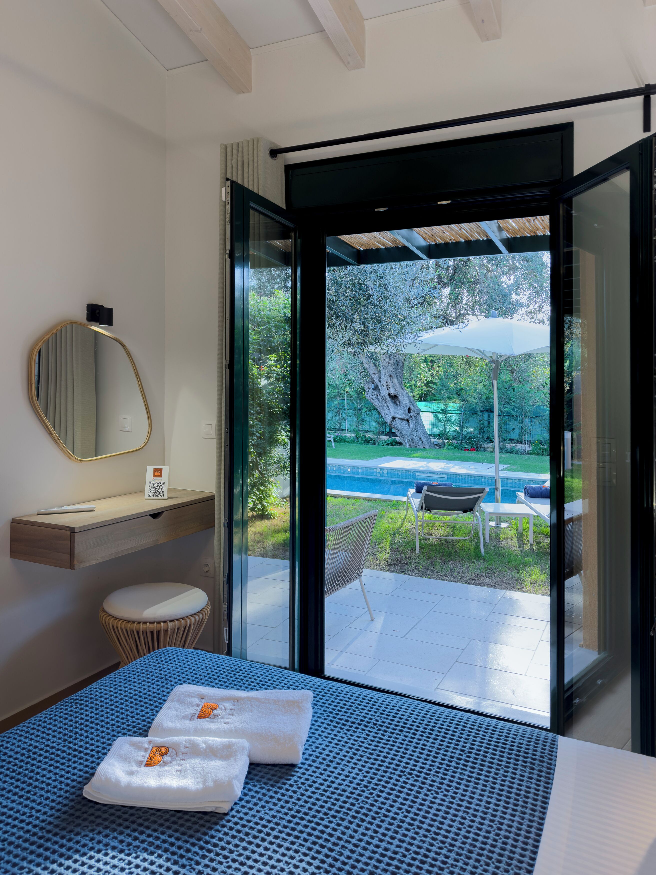 Een moderne hotelkamer met een bed, een klein nachtkastje, een spiegel en uitzicht op een zwembad en tuin.