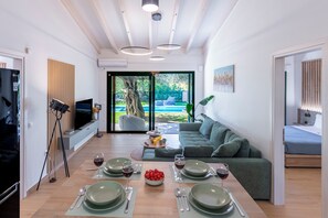 A modern living room with a dining area, a sofa, a TV, and a view of the outdoors. - Galene Eco Luxury Villa Juna (Corfu)