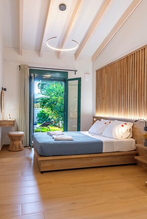 Ein Schlafzimmer mit Bett, Nachttisch, Stuhl, Holzboden und Blick auf einen Garten.