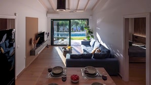 En moderne stue med spiseplads, sofa og udsigt til en pool.