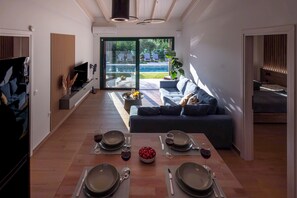 Ein modernes Wohnzimmer mit Essbereich, einer Couch und Blick auf einen Pool.