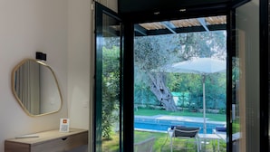 Et moderne hotelværelse med en seng, et lille natbord, et spejl og udsigt til en swimmingpool og have.