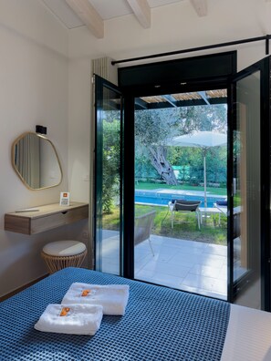 Ein modernes Hotelzimmer mit Bett, Nachttisch, Spiegel und Blick auf Pool und Garten.