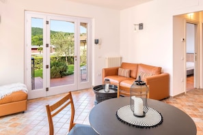 Ein Zimmer mit einer Schiebeglastür, die auf eine Terrasse führt, einem Sofa, einem Tisch mit einem dekorativen Gegenstand und einem Heizkörper.