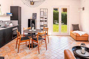 A compact kitchen with a dining area, a sofa, and a view of a garden through a glass door.