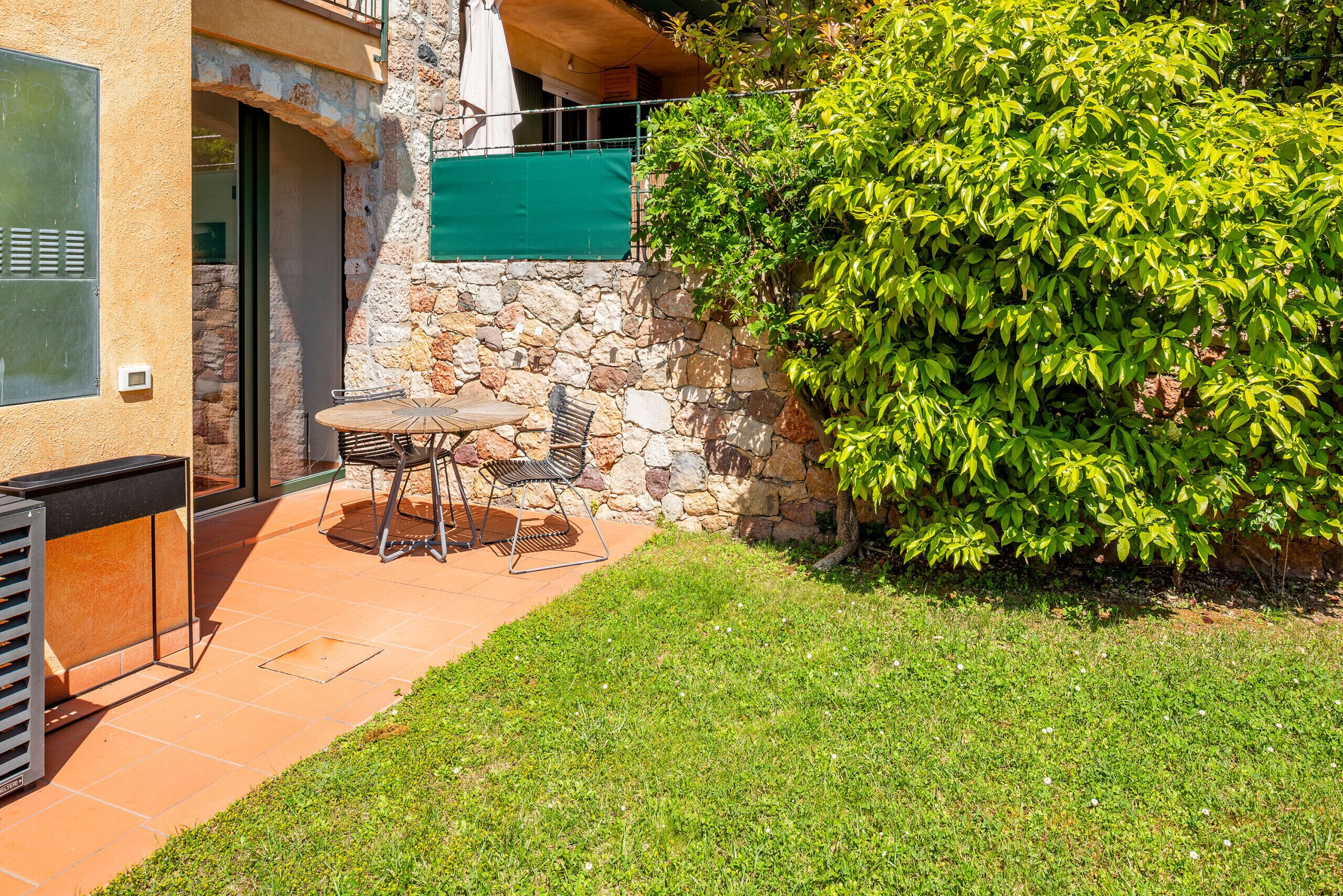 A patio with a table and chairs, a stone wall, and a green bush.