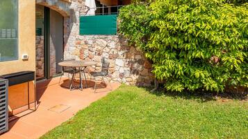 A patio with a table and chairs, a stone wall, and a green bush.