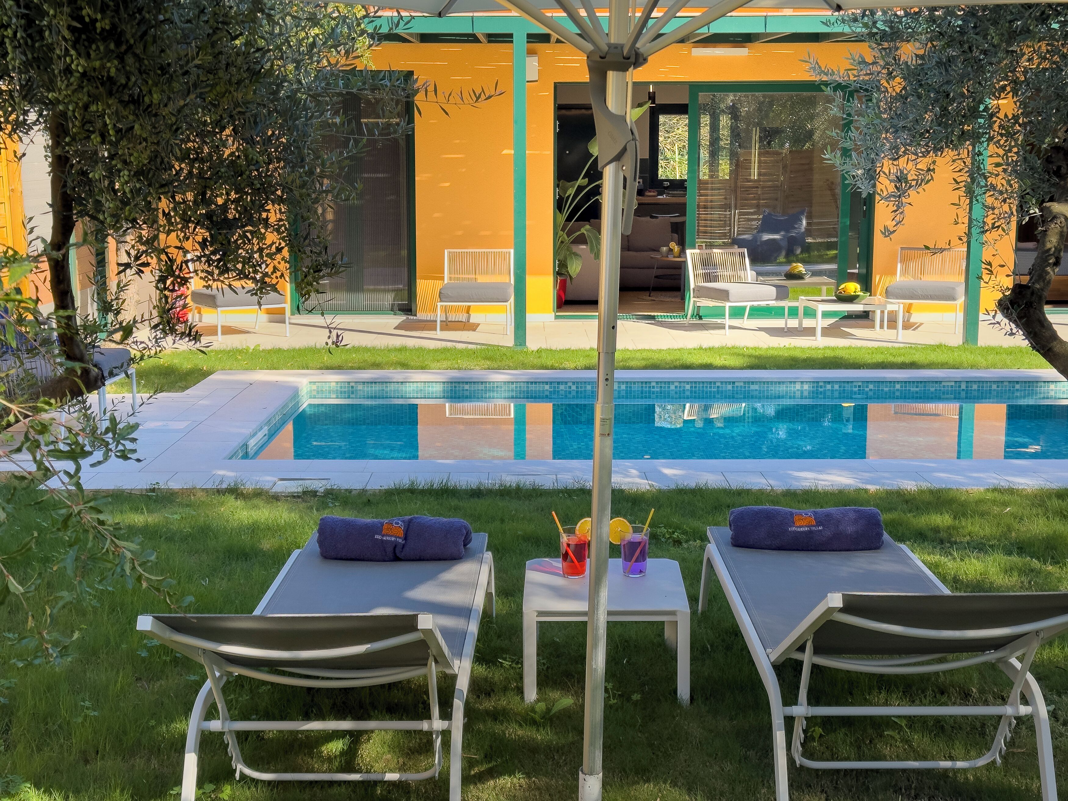 A poolside area with lounge chairs, a small table with drinks, and a view of a building with a yellow facade.