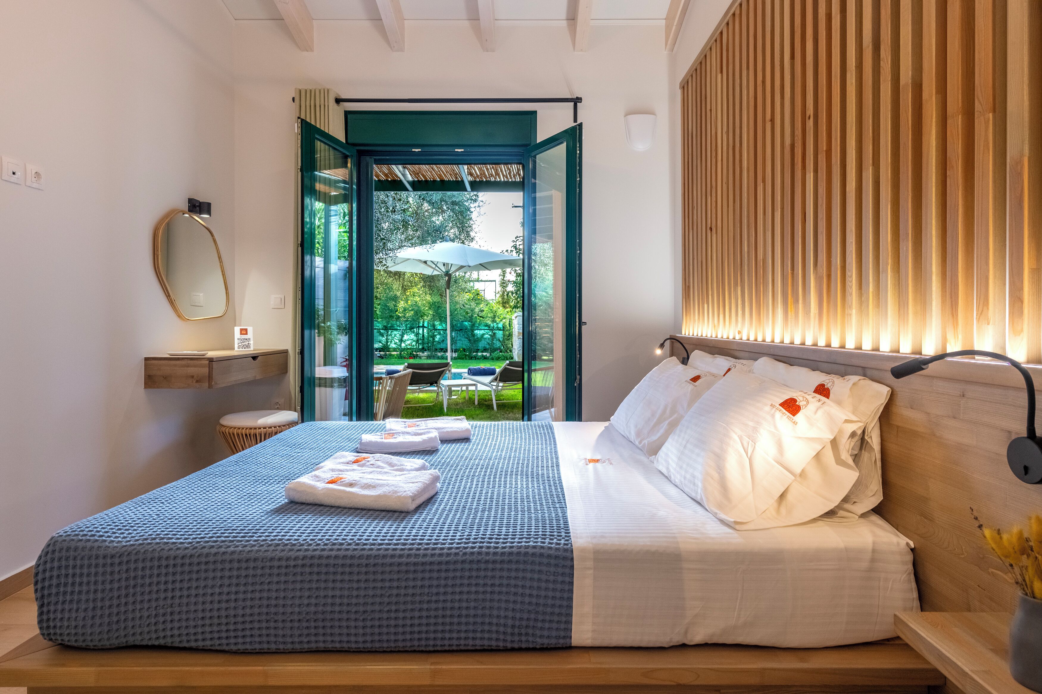 Een slaapkamer met een bed, nachtkastje en uitzicht op een buitenbloemen.