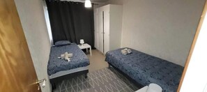 Ein kleiner, kompakter Raum mit zwei Betten, einem Schreibtisch und einem Kleiderschrank.