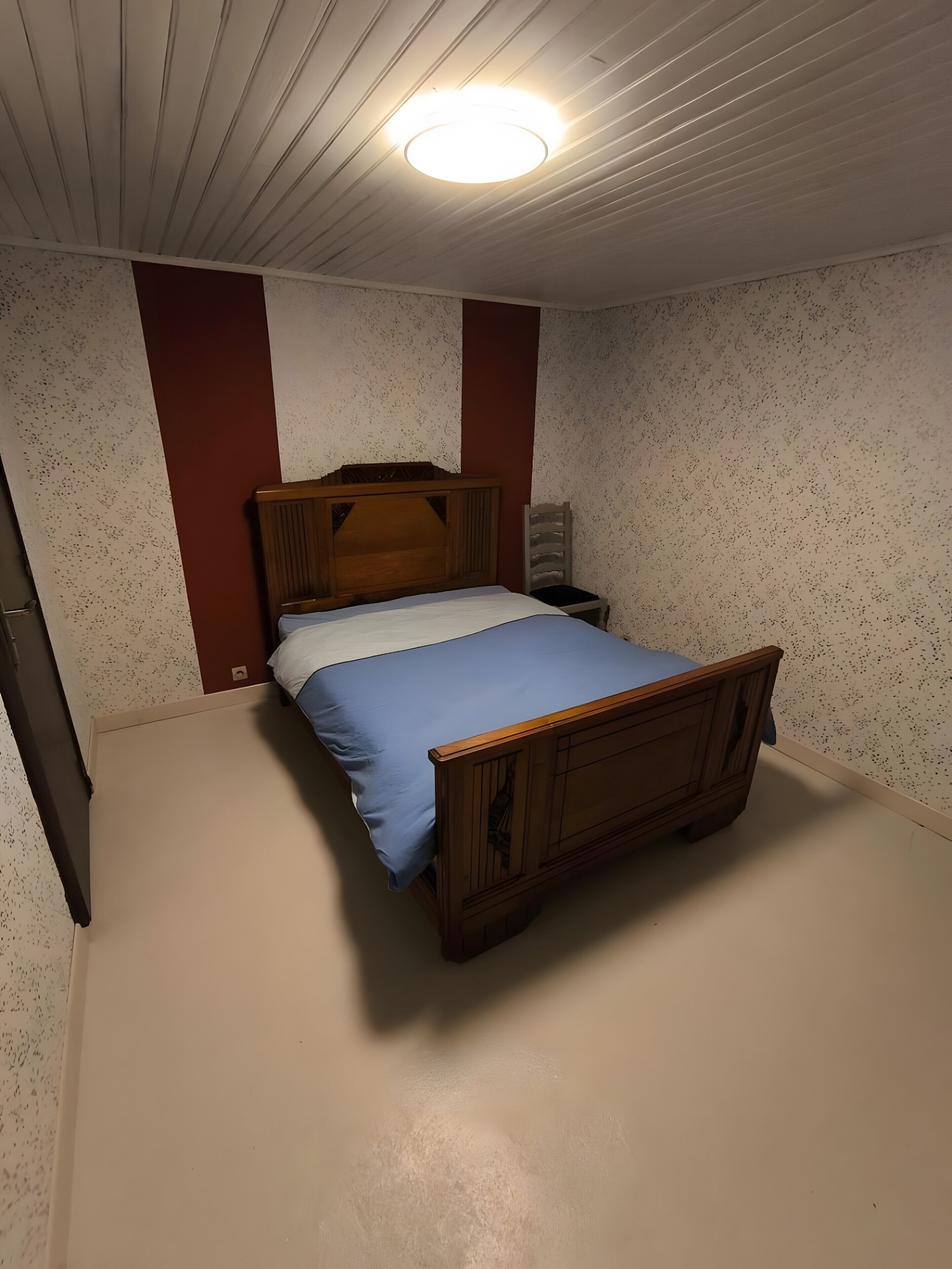 A single bed with a wooden headboard, a nightstand, and a wall with a speckled pattern.