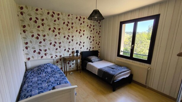 Une chambre avec deux lits, une fenêtre donnant sur un beau paysage, un mur décoré d’un motif et un luminaire suspendu.