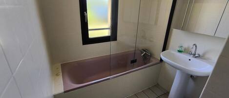 A bathroom with a bathtub, a sink, a window, and a mirror.