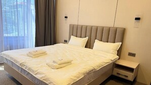 A neatly made bed with white linens and towels, a bedside table, and a nightstand in a hotel room. - Tokyo Hotel (Bishkek)